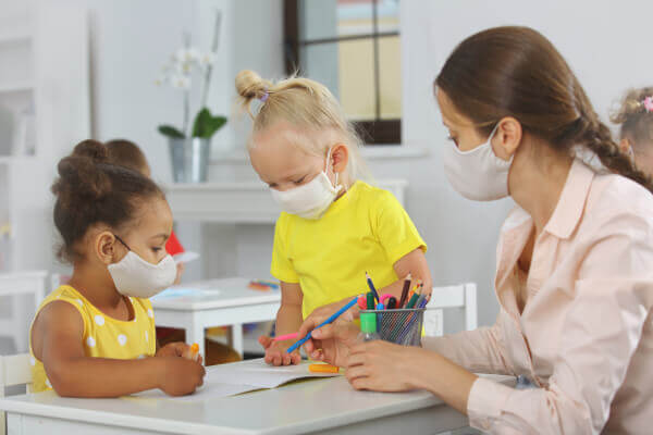 Two children and a teacher wearing face masks while drawing