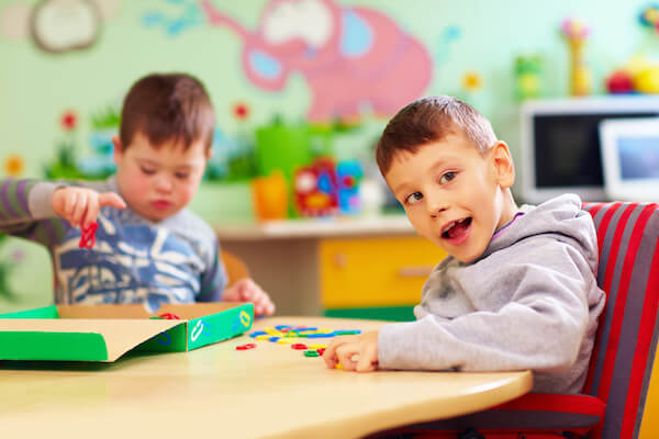 Two children sitting at a table in a classroom playing with colorful, plastic paper clips.