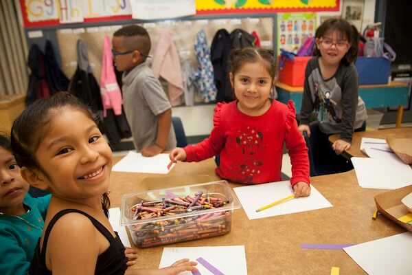 Smiling children drawing and coloring at a classroom table.